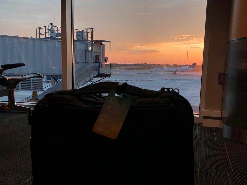 A suitcase in front of an airport window, with a brilliant sunset behind it.