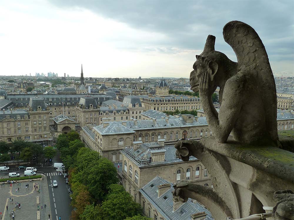 A pensive gargoyle looks out of the rooftops of Paris from the towers of Notre Dame.
