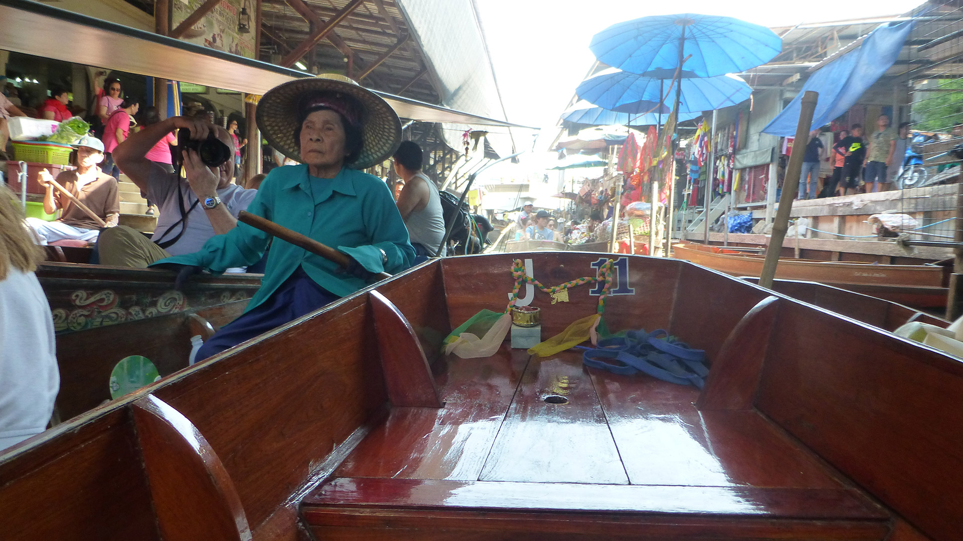 A boat in the floating market in Thailand. A woman in a straw hat paddles another boat nearby.