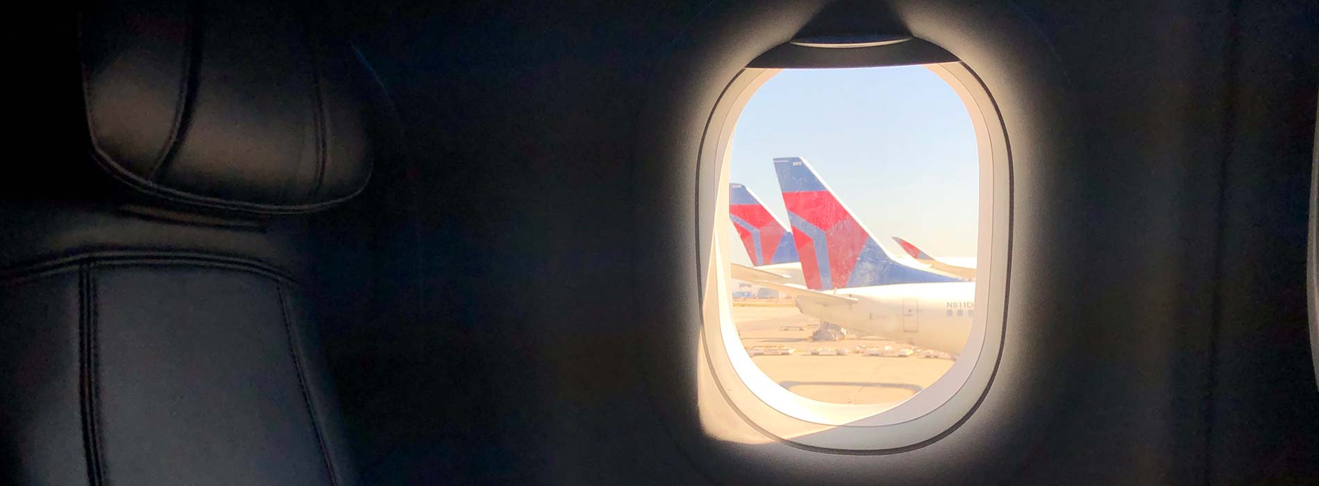 A row of seats on an airplane, the tail of a Delta airplane on the ground out the window.