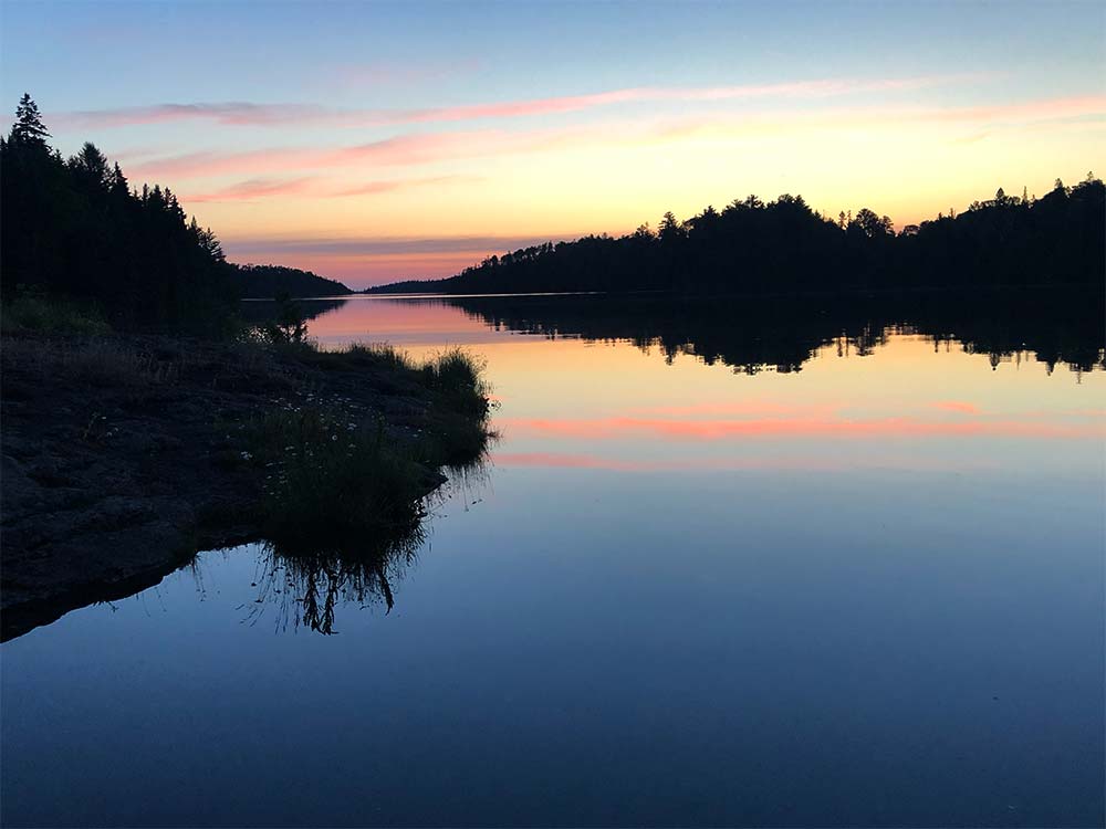 Isle Royale National Park - sunrise at McCargoe cove. The sky is pink, blue, and gold and is reflected in the water.