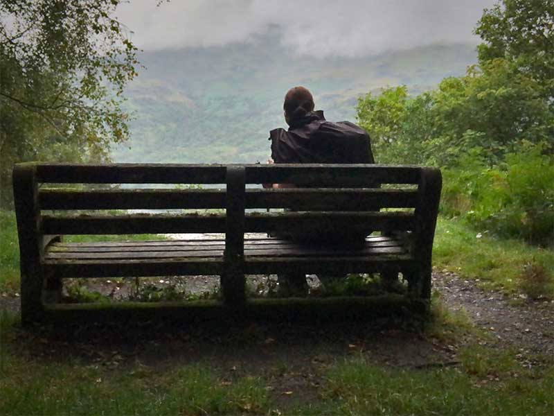West Highland Way hiker sitting on a bench looking at Loch Lomond